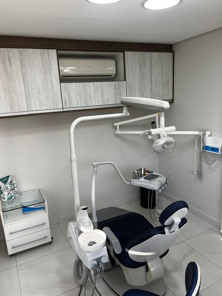 Consultório com cadeira odontológica, equipo e armários de madeira clara